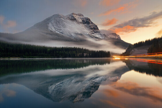 Mountain lake and traffic light trail with reflection and fog at sunset in Banff National Park, Canada.