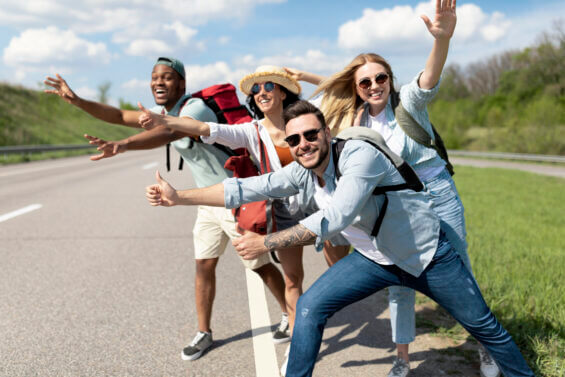 Cheerful young people standing on roadside, stopping car, trying to get free ride, having autostop journey, free space. Exciting travel adventure, hitchhiking with friends, summer holidays