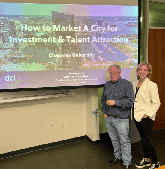 Julie Curtin and Joel Kotkin standing in front of a screen that reads "How to Market A City for Investment and Talent Attraction."