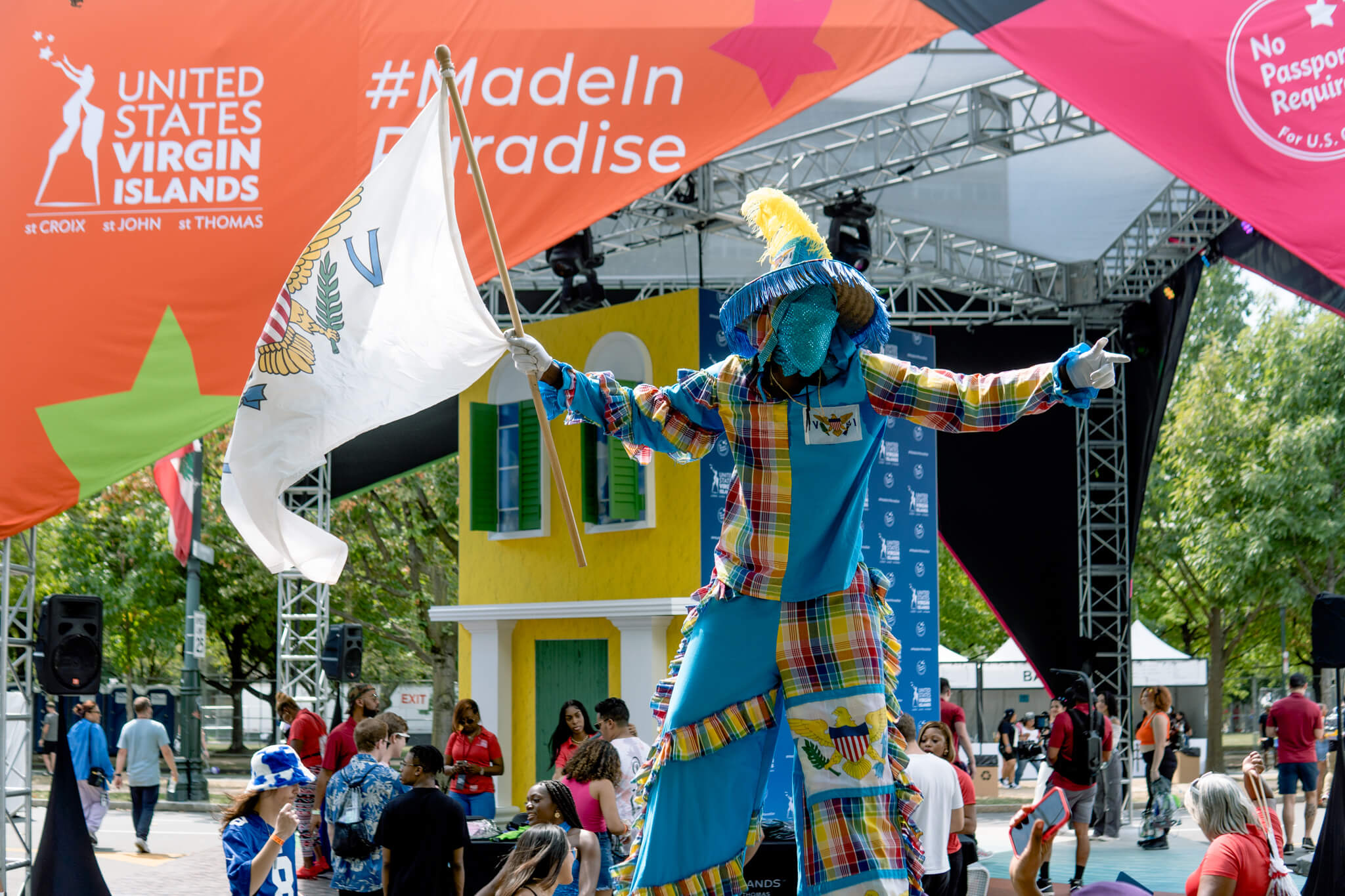 Colorfully dressed performer on stilts waves USVI flag.