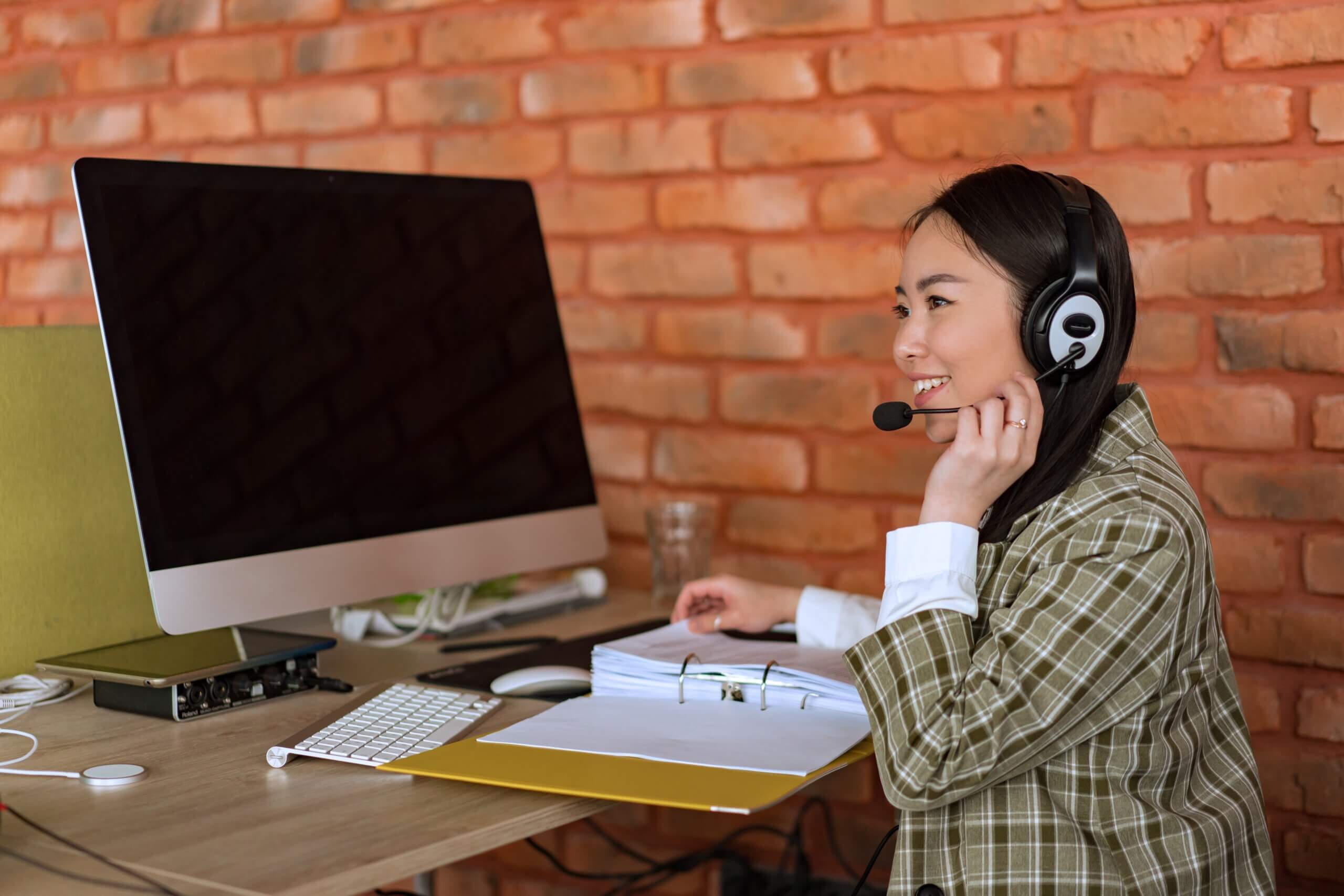 Smiling young female employee speaks with client on headset.