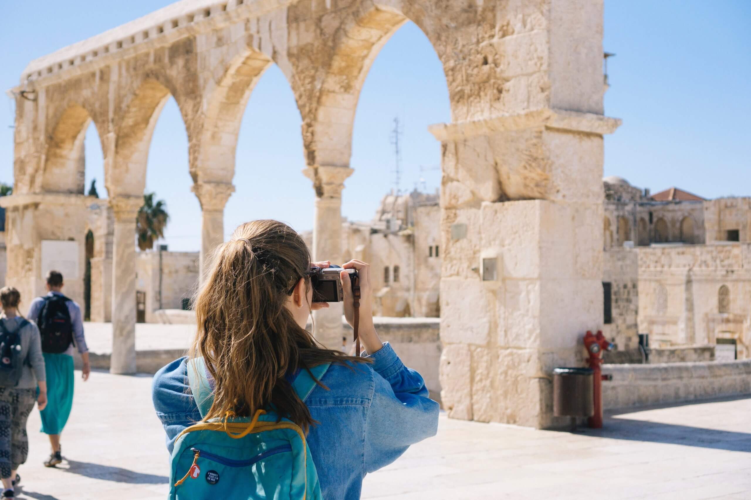 The back of a woman taking a picture of ruins on vacation.