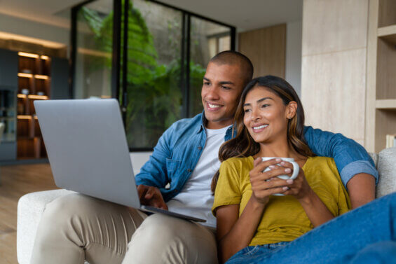 Happy Latin American couple relaxing at home watching movies on their laptop and smiling.