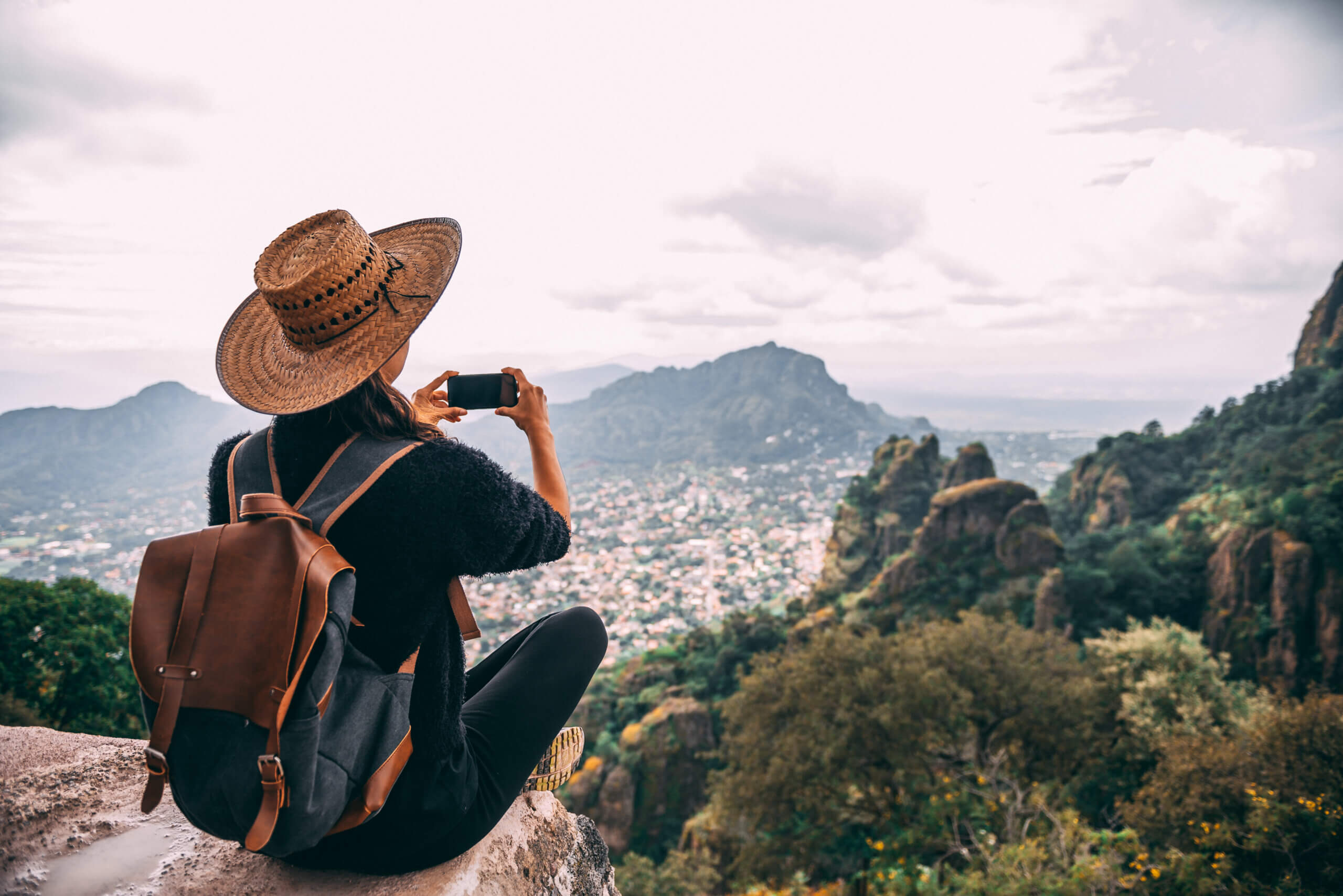 Woman working in influencer marketing in a hat sitting on a rock overlooking Argentina, taking a picture.