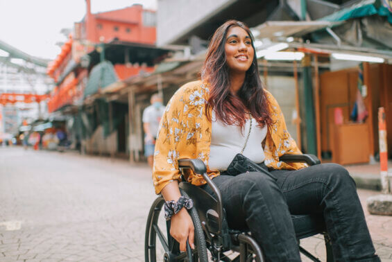 Woman in a yellow shirt pushing her wheelchair down a street.