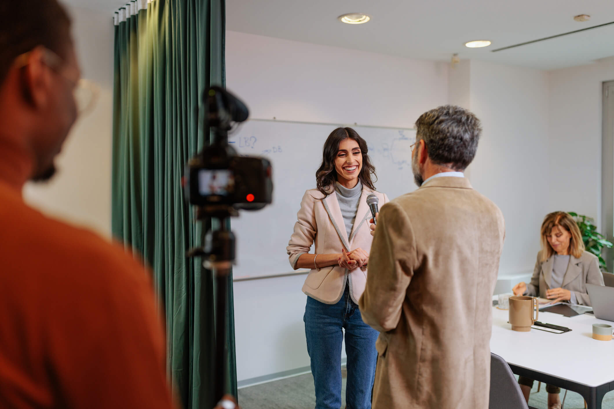 Women in a tan suit jacket and jeans giving a media interview to a man in a tan suit.