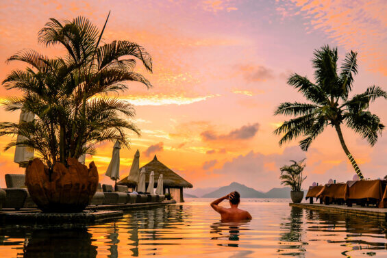 Luxury swimming pool in tropical resort, relaxing holidays in Seychelles islands. La Digue, Young man during sunset by swimpool Seychelles