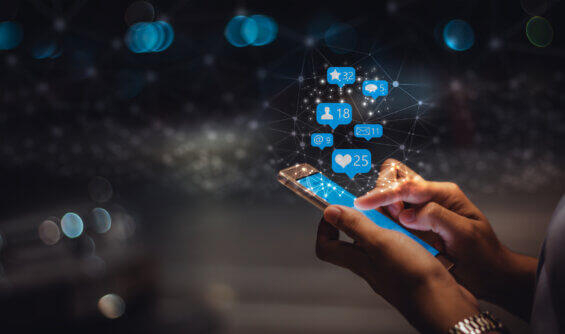 A hand holding a phone that is displaying activity such as likes and shares from advertising on LinkedIn