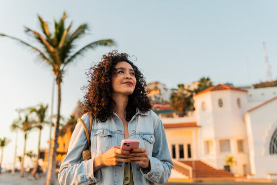 A Latina woman holding a cellphone while looking around outside