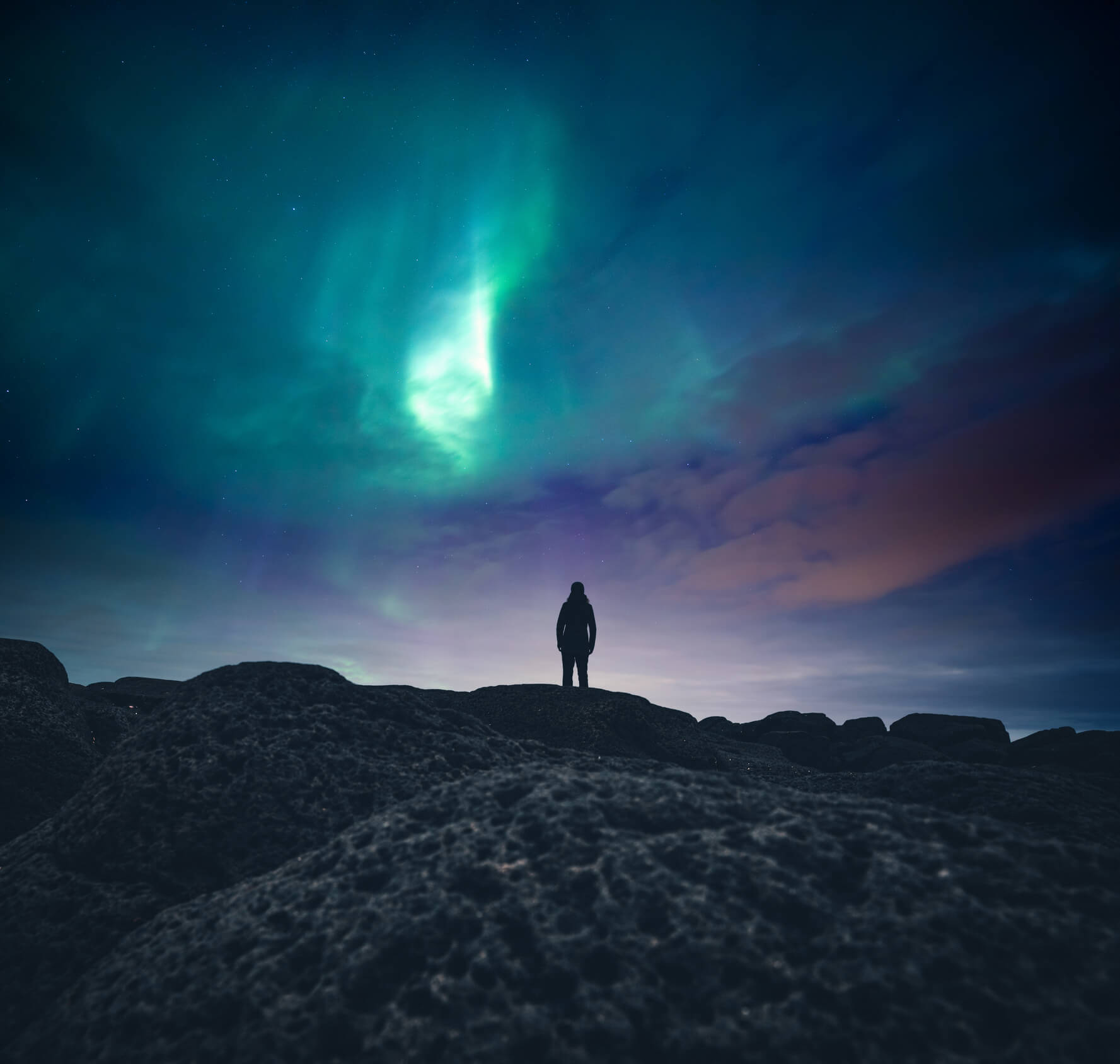 Lone person standing on a hill looking out at Northern Lights.