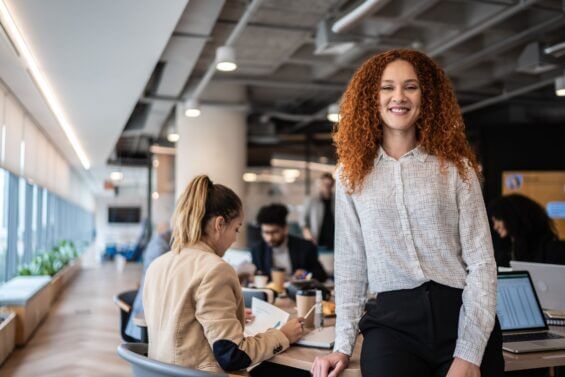 Young woman with red curly hair smiles at camera in the office.