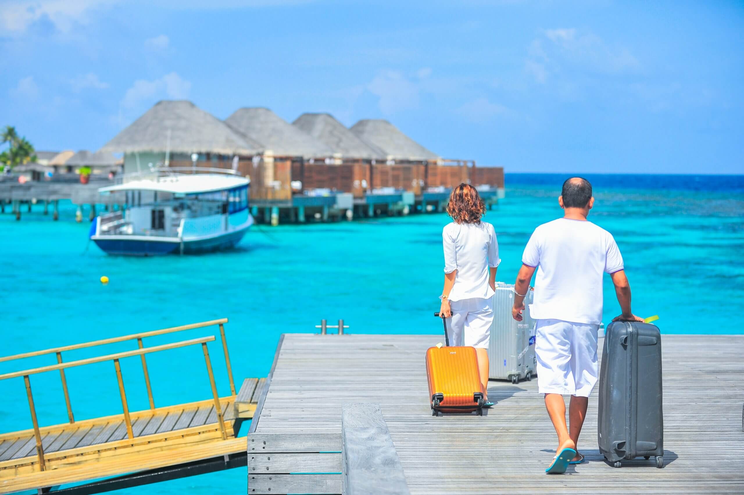 Man and woman walk with their luggage on a luxury hotel's dock.