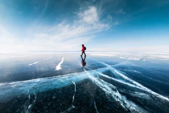 Man in winter backpacking clothes crosses frozen lake.