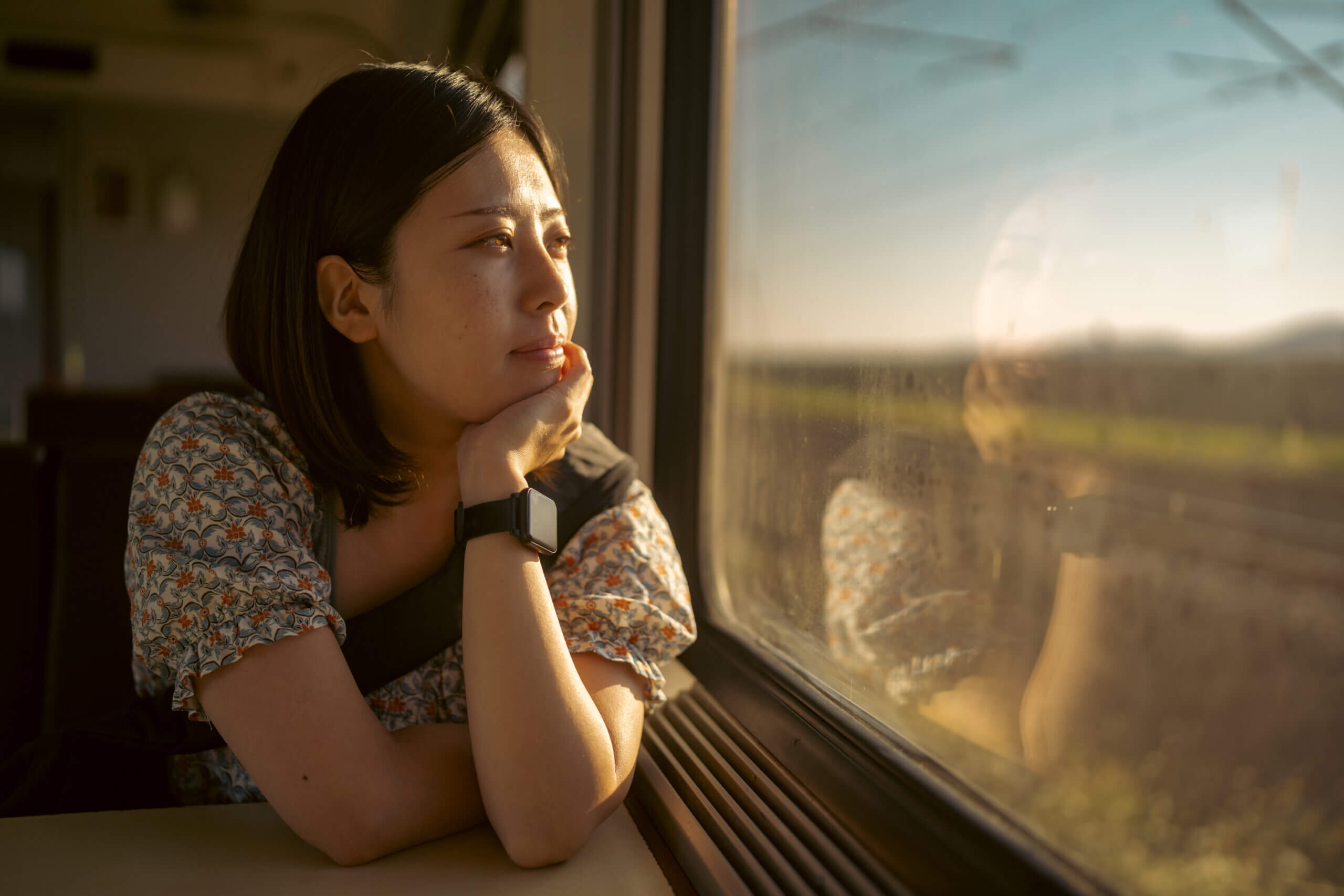 Portrait of a female traveler staring out the window of a train during a sunny afternoon.