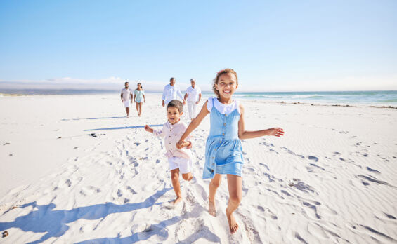 Adorable siblings holding hands while running together on sandy beach